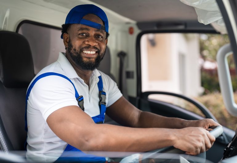 Smiling professional mover in a blue uniform driving a truck, offering junk removal and cleanout services