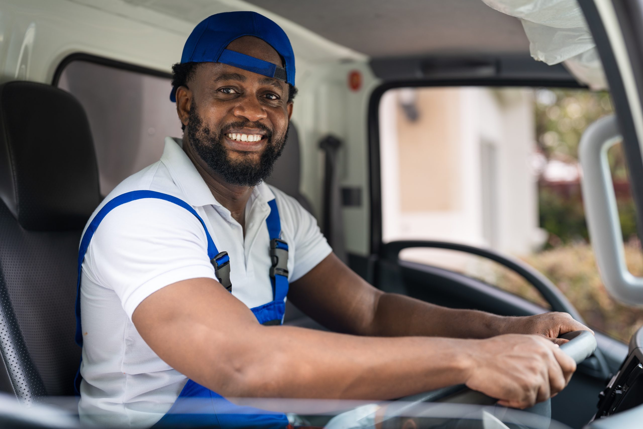 Smiling professional mover in a blue uniform driving a truck, offering junk removal and cleanout services